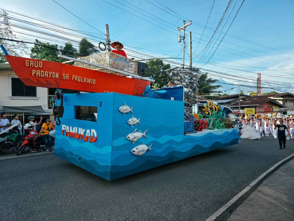 Blue festival float depicting the sea with fish, carrying a red boat on top during Pamukad Festival in Enrique Villanueva