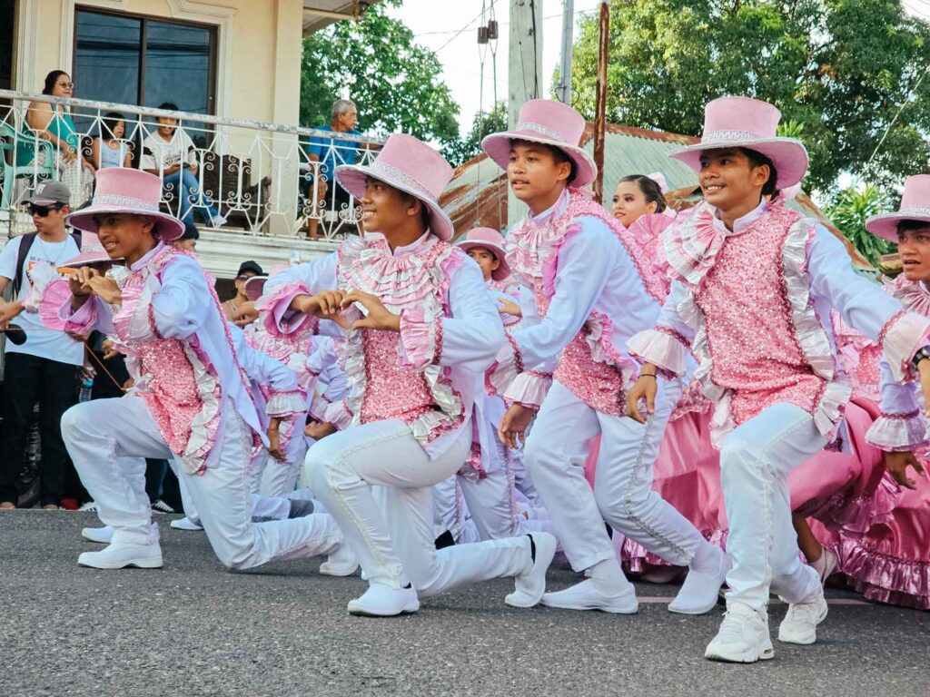 Boys in pink traditional outfits kneeling on the street during a Siquijor fiesta parade, making a heart shape with their hands