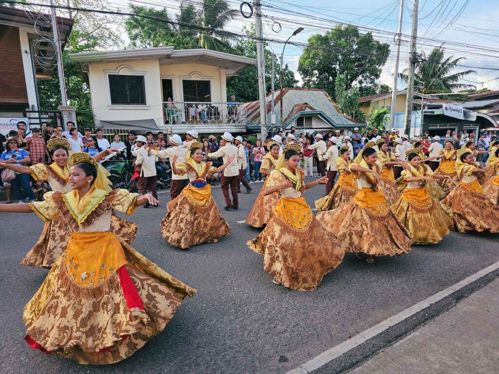 Women in yellow traditional outfits dancing on the street during a Siquijor fiesta, with spectators watching from the sidelines